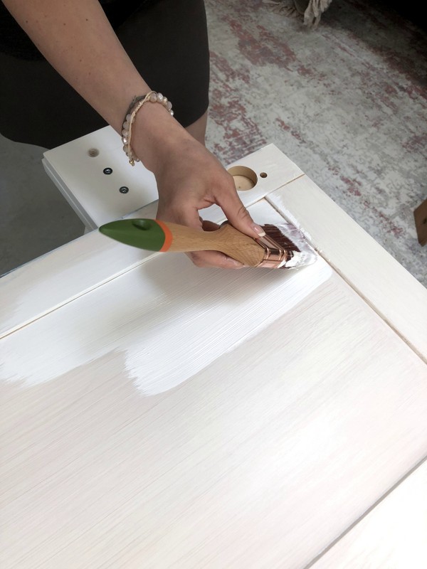 hand holding a paint brush painting white paint on a cabinet