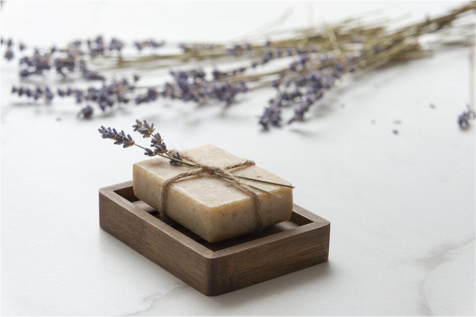 Bar of soap tied with twine and a lavender flower, in the background there is a bouquet of lavender