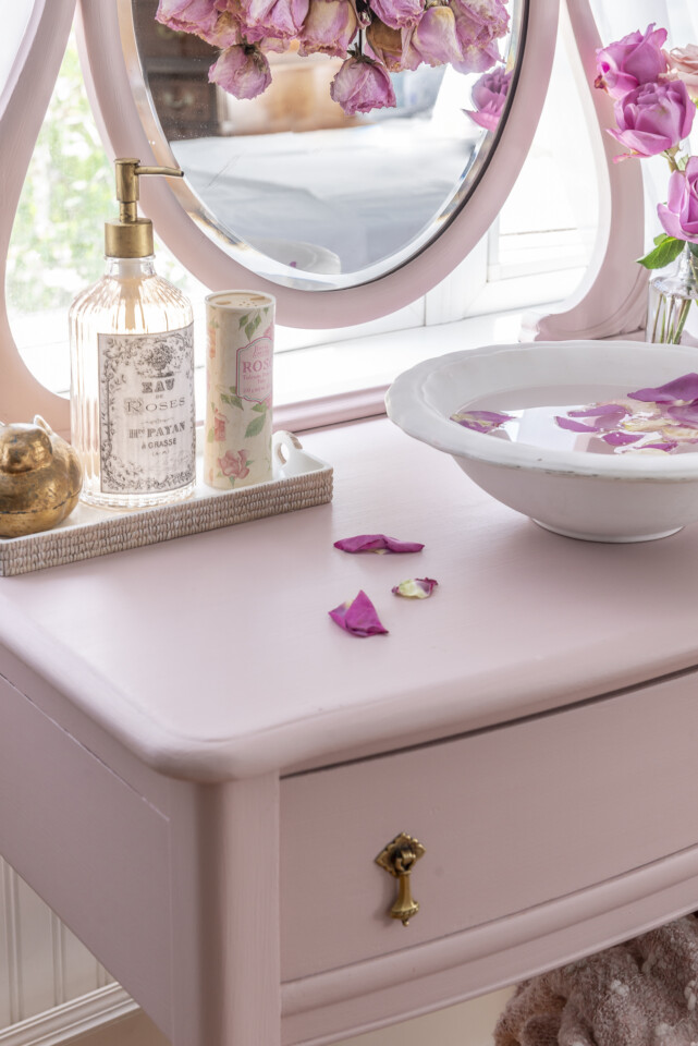 Close up of top of vanity with rose petals, lotion dispenser and bowls with water and floating rose petals