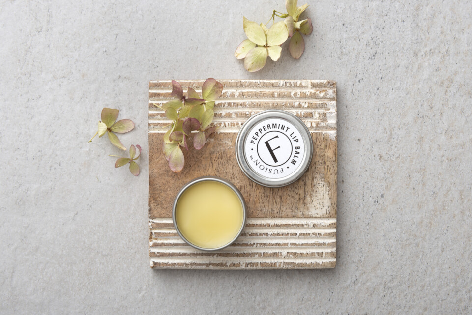Fusion lip balm sitting open on a coaster with a few flowers