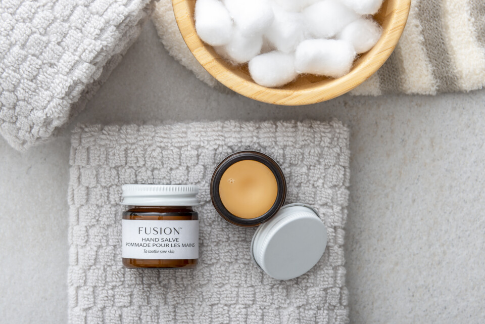 Fusion hand salve laying open on a hand towel next to a bowl of cotton swabs