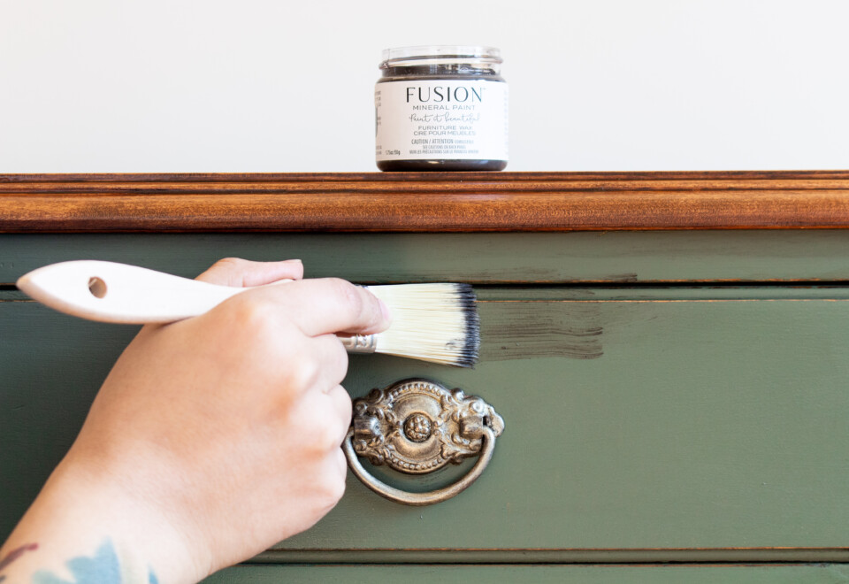 Jar of furniture wax sitting on top of painted dresser, someone is painting a streak of wax across the top drawer
