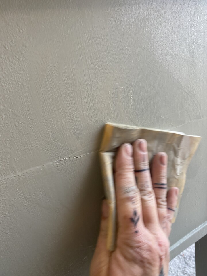A photo of someone's hand wet sanding the side of a dresser