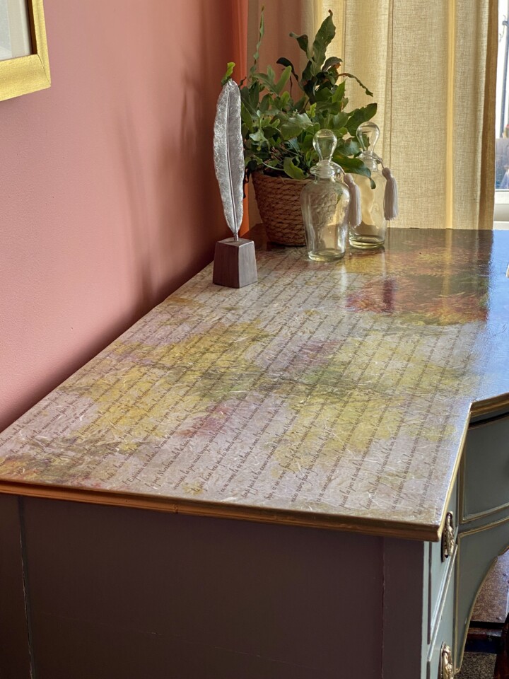 Top angled view of decoupage desk, staged with vases and feather pen