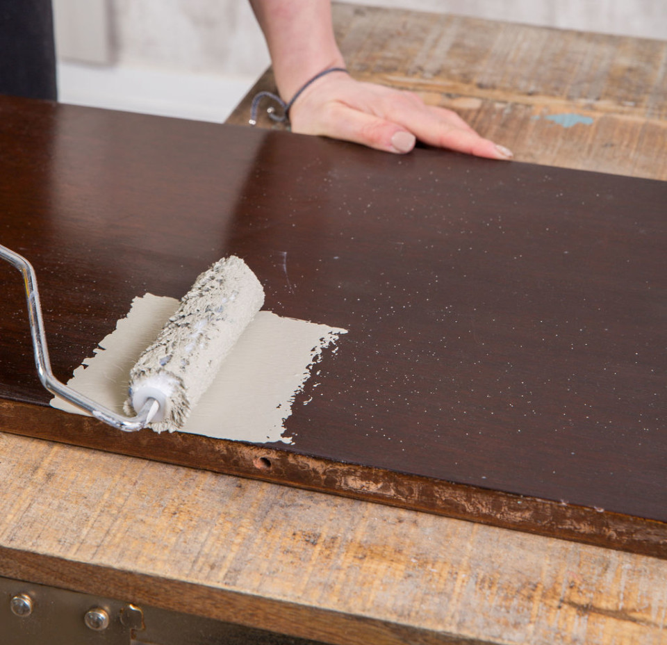 Rolling paint onto a glossy wooden piece of furniture with a microfibre roller