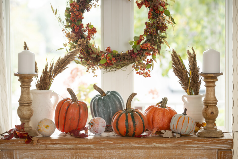 Staged table with a harvest theme, 7 pumpkins, two vases with fall themed flowers and a fall themed wreath hanging behind