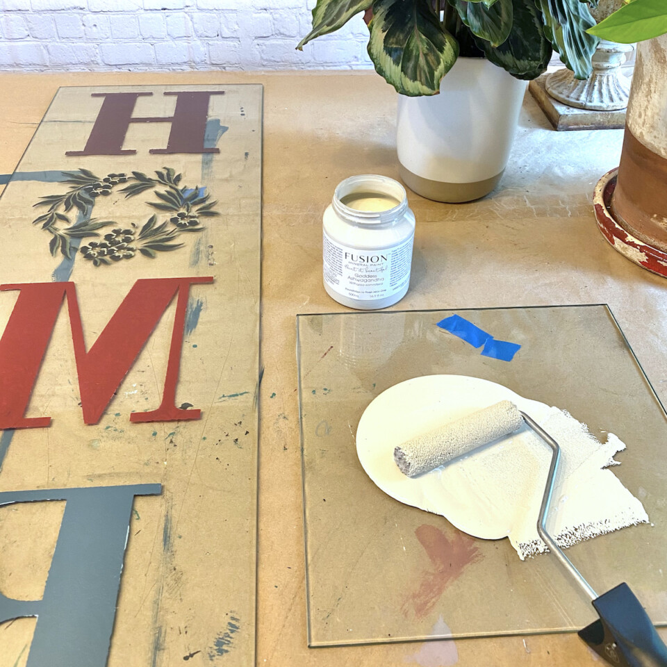 Stencilled letters H-O-M-E with a piece of glass beside it with white fusion mineral paint and a microfibre roller 