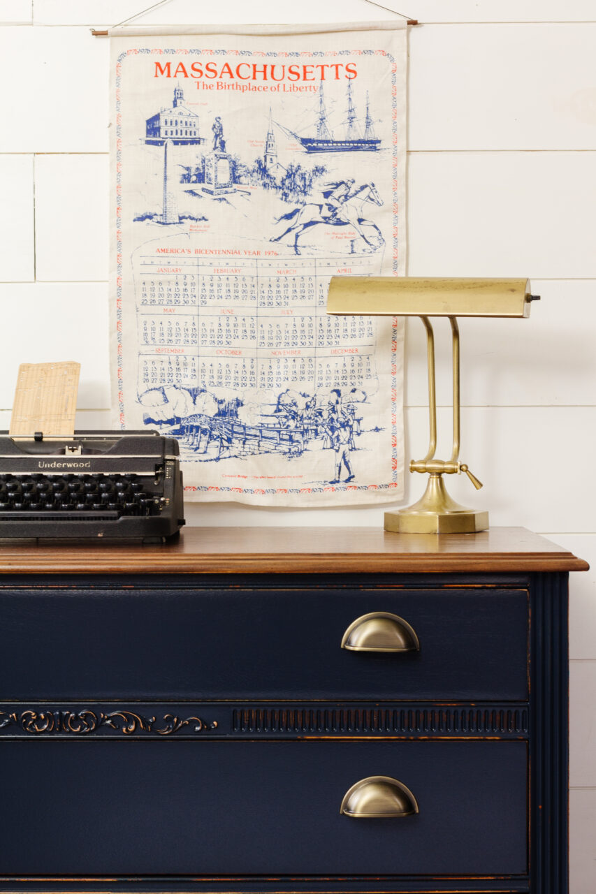 staged dresser painted in midnight blue with plant, books, lamp & typewriter on top