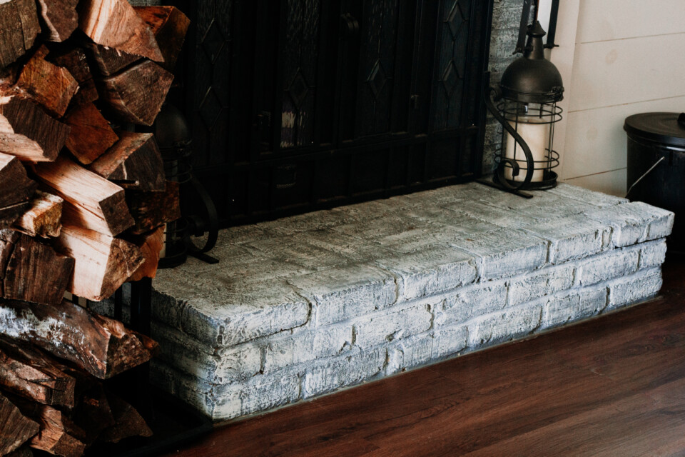 black fireplace with grey brick, stack of firewood beside