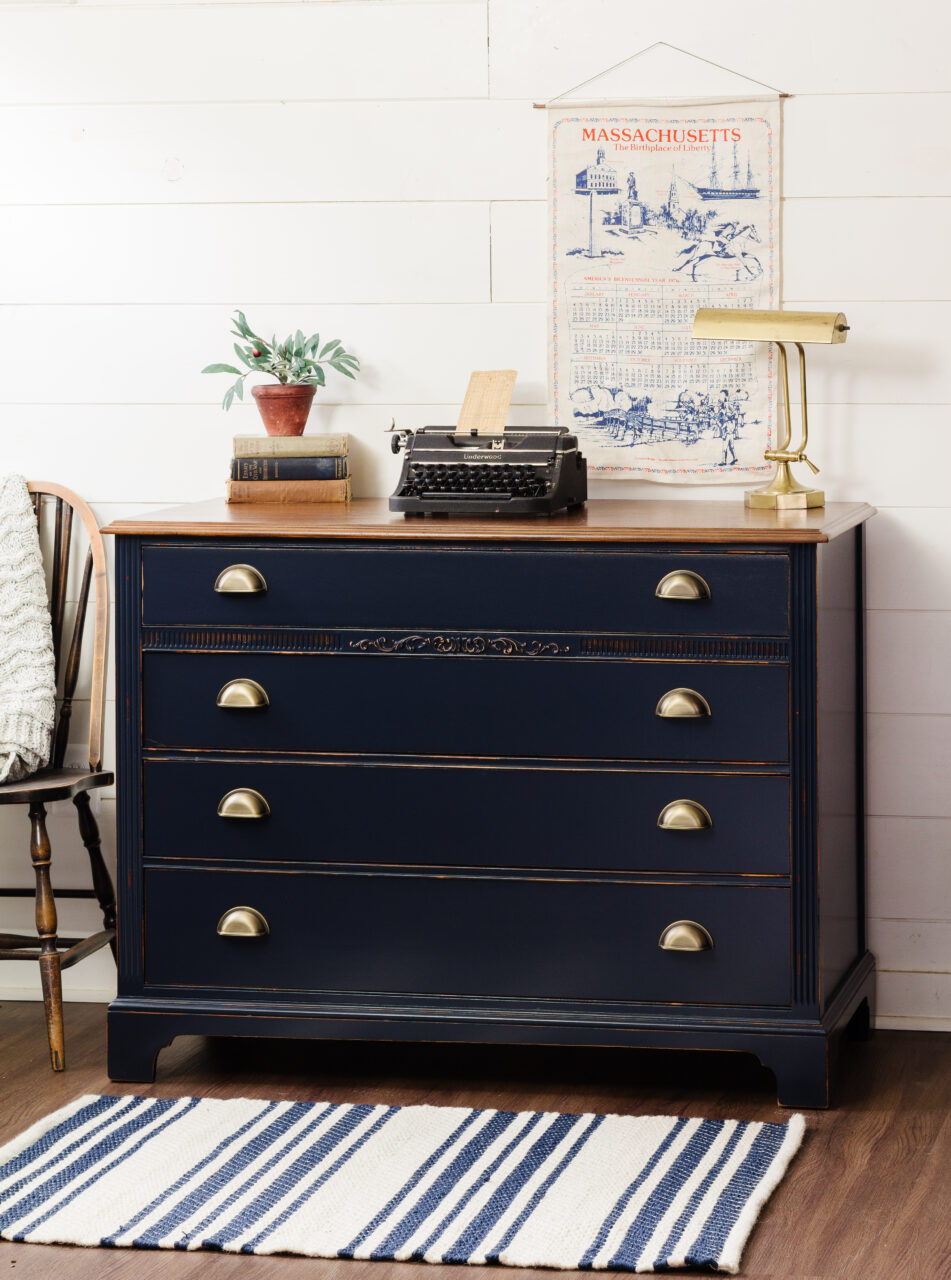 staged dresser painted in midnight blue with plant, books, lamp & typewriter on top