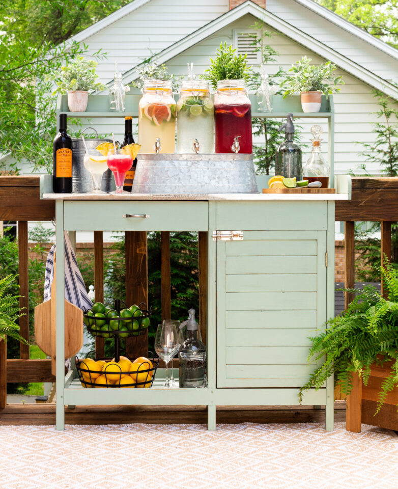 painted bench & staged with alcohol bottles, three drink jugs, potted plants, lemons, limes, cutting boards, etc.,