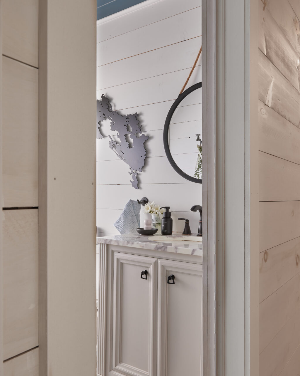 Bathroom door is half closed, through the door you can see a white vanity with marble countertops and black accents.