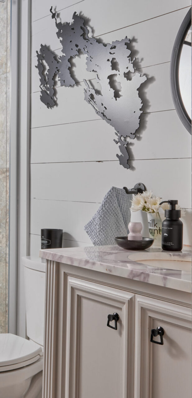 Bathroom with white vanity, black accents, marble countertop, muskoka lakes art piece on the wall