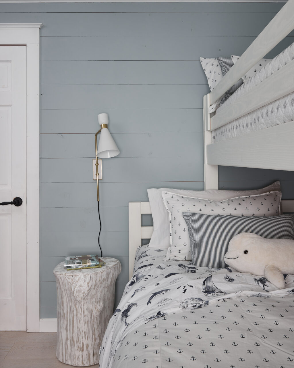 white bunk bed with nautical theme bedding, white seal stuffed animal and white wood stump bedside table