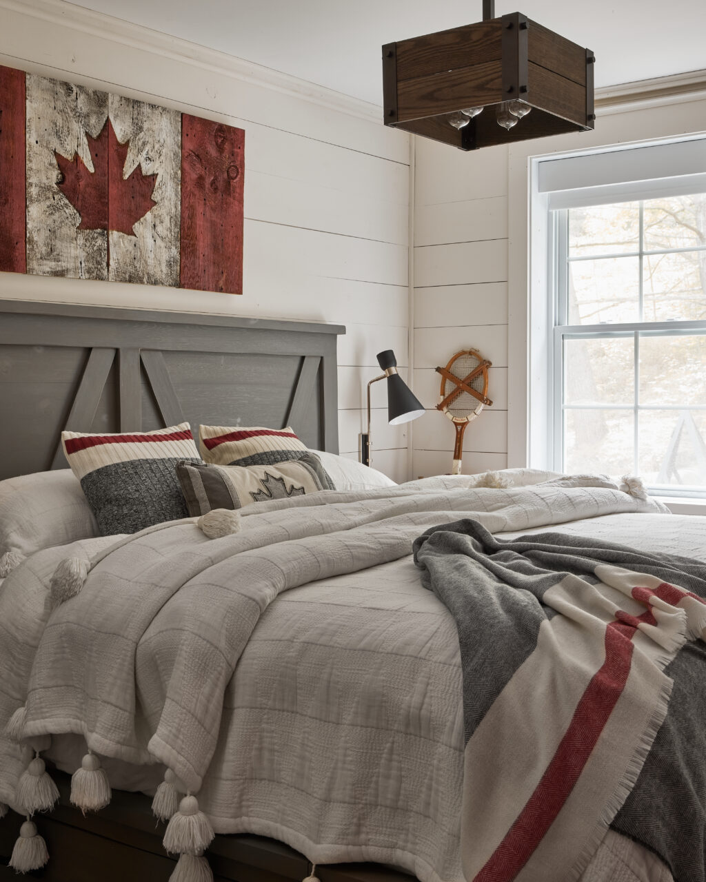 White walled room with roots theme decor (canadian flag above bed, grey and red stripes bedding & grey headboard)